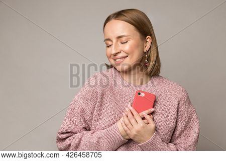 Happy Pleased Woman Hug Smartphone. Young Blond Female Press Mobile Phone To Chest Get Pleasant Mess
