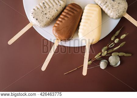Four Popsicles Lying On A Plate On A Brown Table. Top View