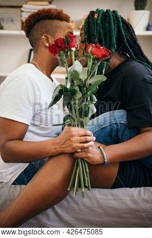 Happy lesbian couple holding roses and kissing in the bedroom