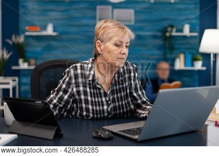 Senior Business Owner Working From Home Office Using Portable Computer. Elderly Woman In Home Living