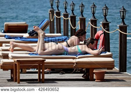 Hisaronu, Turkey - July 2021: Two Girls In Bikini Lying With Smartphones On Tanning Beds On A Beach.