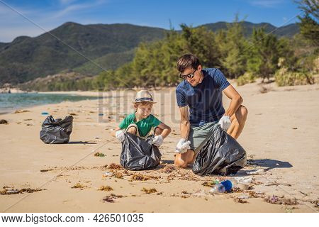 Dad And Son In Gloves Cleaning Up The Beach Pick Up Plastic Bags That Pollute Sea. Natural Education