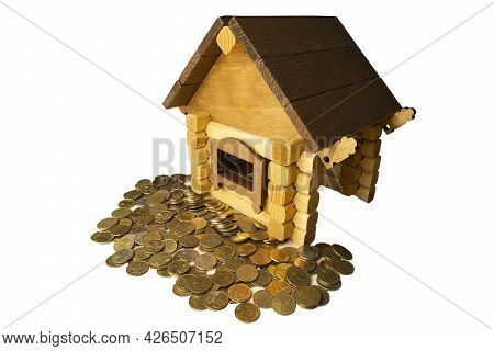 A Miniature Wooden House Stands Next To Metal Coins Isolated On A White Background