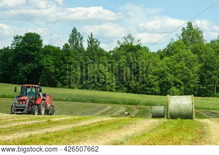 Working On A Tractor In A Field Making Large Rolls Of Hay For Livestock Against The Backdrop Of A Su