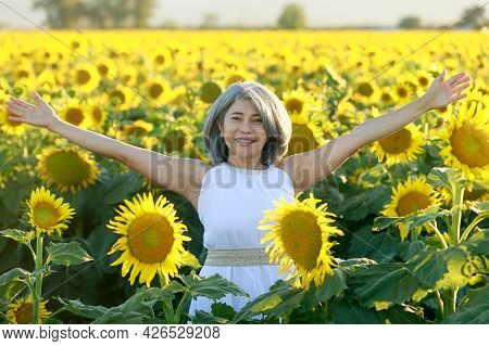 Woman In White Dress Standing With Arms Raised In A Field Of Sunflowers In Summer Bloom. Dixon, Sola