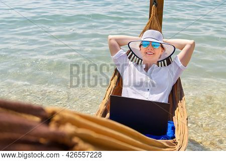 Work From Anywhere. Young Smilyng Woman, Female Freelancer In Straw Hat Working On Laptop On Beach.