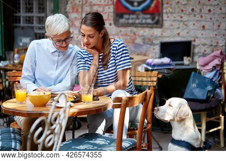 young adult woman reading a book together with elderly caucasian female. Having a good time with her dog beside. mother and daughter relationship concept.