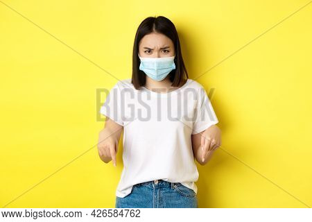 Covid-19, Pandemic And Social Distancing Concept. Disappointed Asian Girl In Medical Mask, Frowning 
