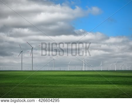 Eolian Farm Renewable Energy In Fresh Green Field Against Clear Blue Sky