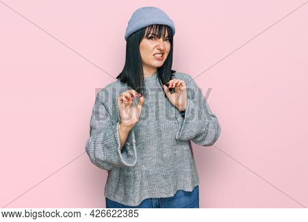 Young hispanic woman wearing cute wool cap disgusted expression, displeased and fearful doing disgust face because aversion reaction. with hands raised 