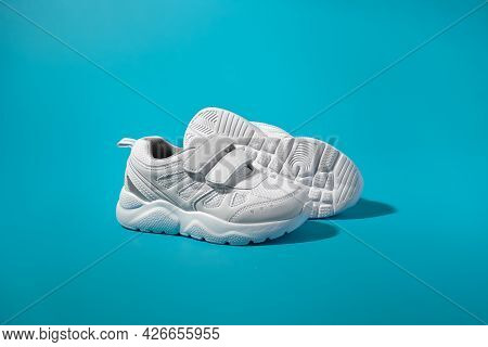 Side View Of Two White Teen Sneakers With Velcro Standing In Front Of The Sole Of Another Sneaker On