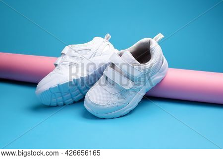 Two White Teen Sneakers With Velcro Fasteners For Comfortable Footwear On A Pink Long Paper Roll On 