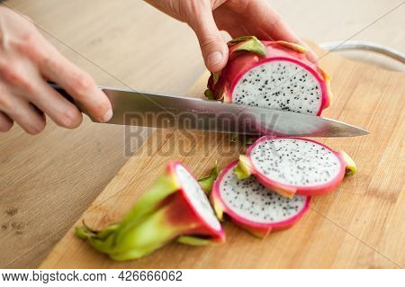 Female Hands Is Cutting A Dragon Fruit Or Pitaya With Pink Skin And White Pulp With Black Seeds On W