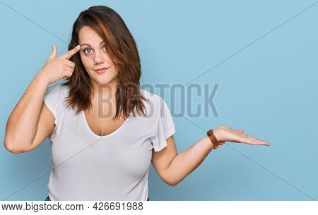 Young plus size woman wearing casual white t shirt confused and annoyed with open palm showing copy space and pointing finger to forehead. think about it. 