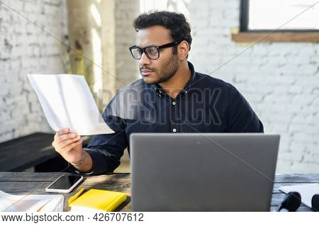 Executive Mixed-race Male Office Employee Doing Paperwork Sitting At The Desk With Laptop In Office,