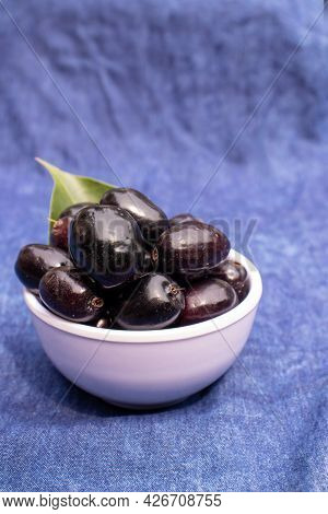 Closeup Of Organic Malabar Plum Or Jamun In A Bowl Isolated On Blue Fabric Background With Leaf In V