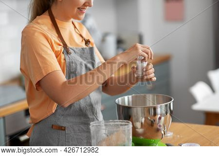 culinary, baking and people concept - happy smiling young woman cooking food on kitchen at home and adding salt
