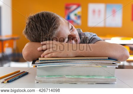 Tired caucasian schoolboy sitting at desk in classroom sleeping on a pile of schoolbooks. childhood and education at elementary school.