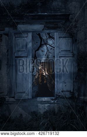 Scary Halloween Witch Standing In Old Damaged Wood Window With Wall Over Church, Birds, Dead Tree An