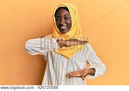 Beautiful african young woman wearing traditional islamic hijab scarf gesturing with hands showing big and large size sign, measure symbol. smiling looking at the camera. measuring concept. 