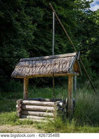A Vintage Wooden Well. Green Grass And Forest In Background.