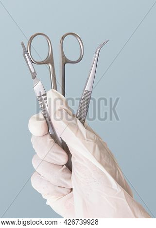 Gloved hand holding stainless steel medical instruments