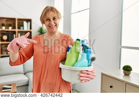 Middle age blonde woman holding cleaning products cleaning at home pointing finger to one self smiling happy and proud 