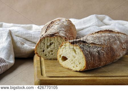 Bread Loaf, Cut Into Two Pieces, On Wooden Cutting Board. Baked Bread And Dish Towel On Craft Paper,