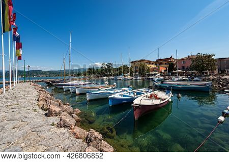 Port Of The Small Village Of Cisano With Small Boats Moored, Tourist Resort On The Coast Of Lake Gar