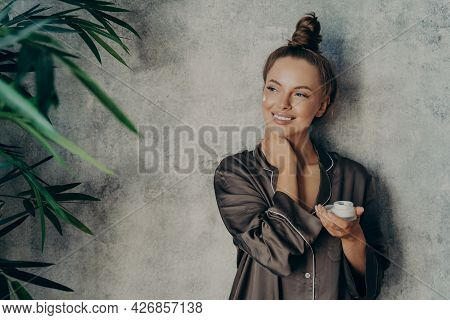 Young Beautiful Woman With Glowing Healthy Skin Broadly Smiling While Holding Moisturizing Face Crea