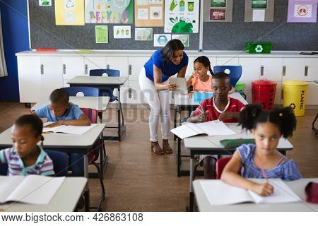 African american female teacher with digital tablet teaching a girl at elementary school. school and education concept