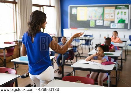 Rear view of african american female teacher teaching students in the class at elementary school. school and education concept