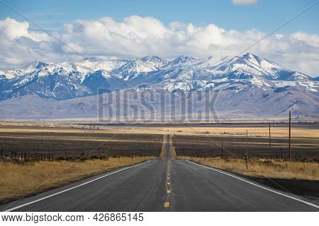 A Long, Straight Road Heading Into The Distant Mountains In Idaho.