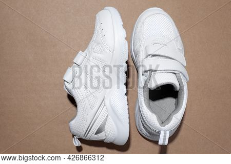 Top View White Kid Sneakers With Velcro Fasteners, One Sneaker On The Side Isolated On A Beige Craft