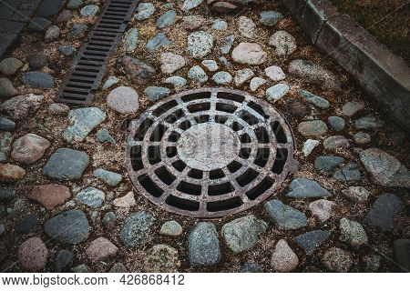 An Old Metal Sewer Manhole Among The Cobblestones. Valdai. Novgorod Region. Russia. May 2021