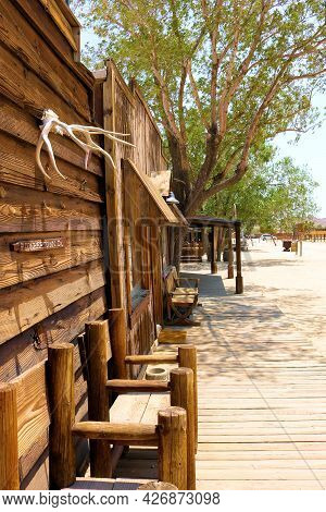 July 14, 2021 In Pioneertown, Ca:  Rustic Chairs On A Wooden Boardwalk Besides Historical Buildings 