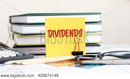 A Yellow Card With The Text Dividends Stands On A Clip For Papers On The Desk Against The Background