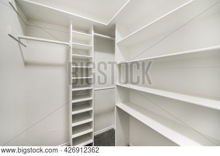 Small Empty Walk In Closet With White Interior And Built In Shelving Units