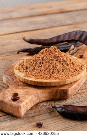 Dry Carob Pods And Carob Powder Over Wooden Background