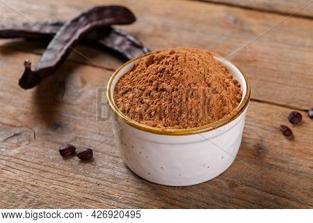 Dry Carob Pods And Carob Powder In A Bowl Over Wooden Background