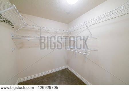 Interior Of A Windowless Walk In Closet With Brown Carpet Flooring