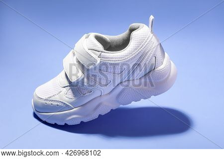 Side View One Flying White Child Sneaker With Velcro Fasteners Simulating A Walk Isolated On A Purpl