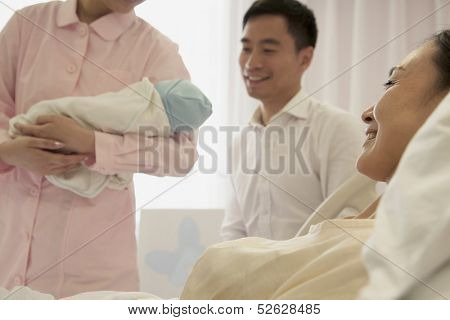 Nurse holding newborn baby in the hospital with mother and father