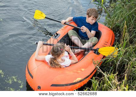 Brother and sister in a rubber boat floating in a pond with reed