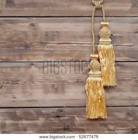 Gold rope with curtain tassel against wooden wall