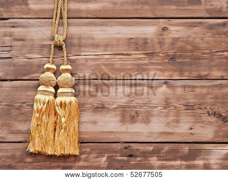 Gold rope with tassel against wooden wall