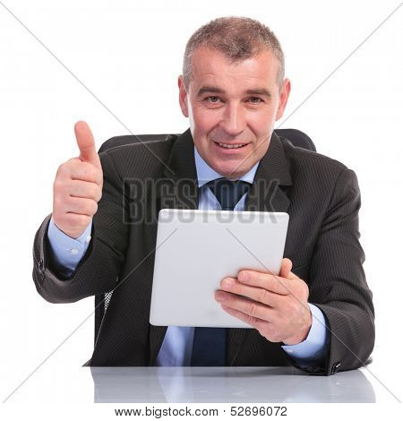 business man at the desk, holding his tablet and showing the thumb up gesture to the camera. on a white background