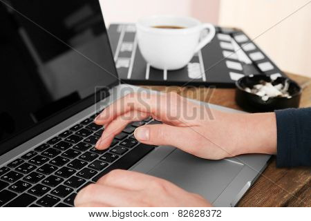 Female hands of scriptwriter working on laptop at desk on cupboard background