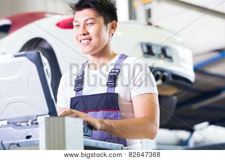 Asian Chinese car mechanic checking auto engine with diagnostics tool in his workshop
