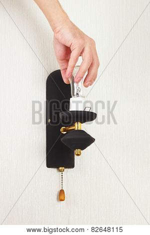 Hand unscrews bulb in a lamp on white wall